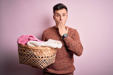 Genç, beyaz, ev işi yapan yakışıklı bir adam çamaşır sepeti sepetinin kapağını tutarken ağzı utançla kaplanmış, korkunun ifadesi, sessizlikten korkmak, gizli konsept.