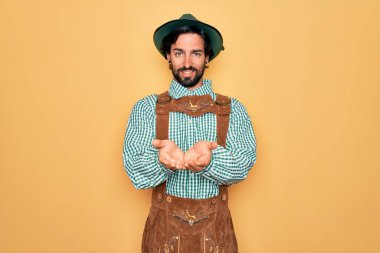Almanya festivali için geleneksel Alman Ekim Festivali kıyafeti giyen yakışıklı genç adam avuçlarını birbirine uzatarak gülümsüyor ya da jest yapıyor. Tutun ve koruyun