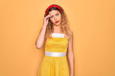 Sarı arka planda dikilip duran mavi gözlü güzel sarışın kadın. Alnındaki sorun yüzünden endişeli ve stresli. Kriz için endişeli.