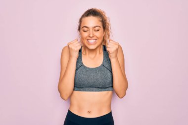 Mavi gözlü genç, güzel sarışın spor kadın spor kıyafetleri giyiyor. Kolları havada ve gözleri kapalı zaferi kutlarken gülümsüyor. Kazanan konsept.