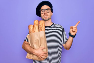 Mavi gözlü genç fırıncı Fransız beresi takıyor. Yanında ekmek çantası var. Çok mutlu bir şekilde elini ve parmağını kenarı işaret ediyor.