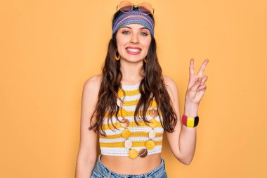 Mavi gözlü, aksesuar takan ve güneş gözlüğü takan genç, güzel hippi kadın iki numaralı parmaklarıyla işaret ederken kendinden emin ve mutlu bir şekilde gülümsüyor..