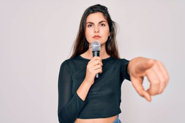 Genç, güzel şarkıcı kız, izole edilmiş arka planda müzik mikrofonuyla şarkı söylüyor. Kamerayı işaret ediyor ve sen, el işareti, ön taraftan pozitif ve kendinden emin bir hareket.