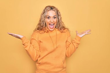 Sarı arka plan üzerine sıradan bir tişört giyen genç ve güzel sarışın kadın çılgın ve başarıyı kollarını kaldırıp heyecanla haykırarak kutluyor. Kazanan konsept