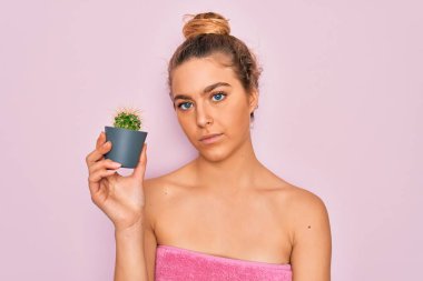 Mavi gözlü güzel sarışın kadın banyo üstüne duş alıyor. Elinde küçük bir kaktüs tutuyor. Yüzünde kendinden emin bir ifade var.