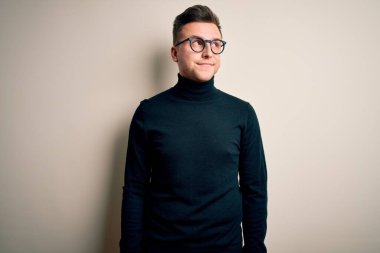 Gözlüklü, sıradan bir süveter giyen genç, yakışıklı beyaz bir adam izole edilmiş arka planda gülümsüyor ve diğer tarafa bakıyor..