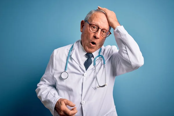 Starszy Siwy Lekarz Noszący Stetoskop Płaszcz Medyczny Niebieskim Tle Zaskoczony — Zdjęcie stockowe