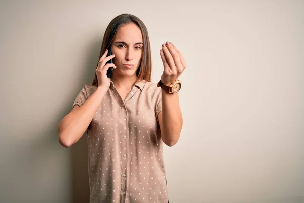 白い背景の上にスマートフォンで会話をしている若い美しい女性手と指でイタリアのジェスチャーを行う自信を持って表現 — ストック写真