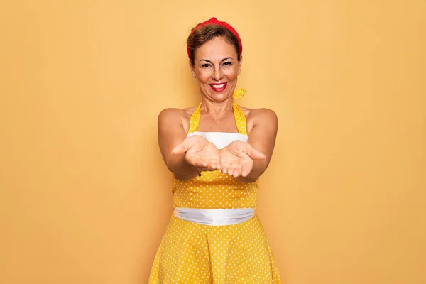 中年妇女穿着50年代风格的复古服装 背景是黄色的 双手合十手心微笑着接受或给予的姿态 扣留和保护 — 图库照片
