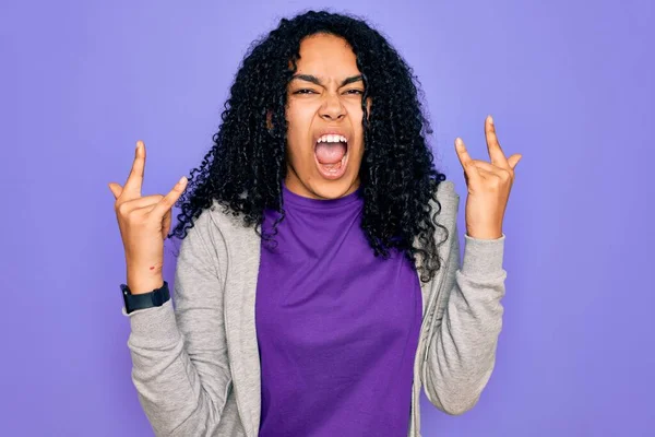 紫色の背景にカジュアルなスウェットシャツを着た若いアフリカ系アメリカ人のスポーティな女性が手を上げてロックシンボルをやってクレイジーな表情で叫んでいます 音楽スター 重い概念 — ストック写真