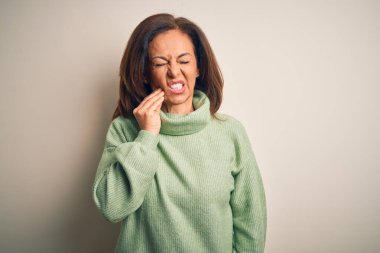 Orta yaşlı, güzel bir kadın diş ağrısı ya da diş ağrısı yüzünden izole edilmiş beyaz arka plan üzerine balıkçı yaka kazak giyip ağıza dokunuyor. Dişçi