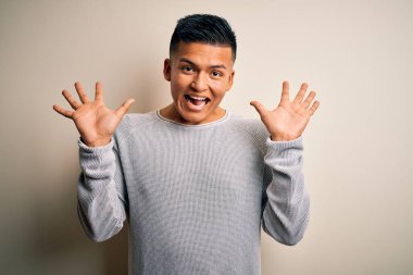 Genç, yakışıklı, latin bir adam izole edilmiş beyaz arka planda dikilmiş çılgın ve başarıyı kollarını kaldırıp heyecanla haykırarak kutluyor. Kazanan konsept