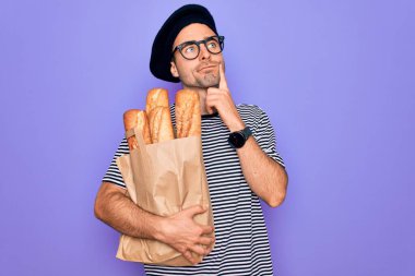 Mavi gözlü yakışıklı fırıncı Fransız beresi takıyor. Elinde ekmek çantası var. Yüzünde ciddi bir ifade var.