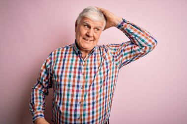 Üst düzey yakışıklı, parlak gömlekli, soyutlanmış pembe arka planda, kendine güvenen, el hareketleriyle saçlara dokunan, çekici ve modaya uygun poz veren bir adam.