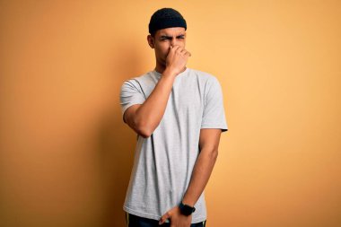 Yakışıklı Afro-Amerikan sporcusu sarı arka planda spor kıyafetleri giyerek spor yapıyor pis ve iğrenç bir koku alıyor, nefesini burnunda tutuyor. Kötü kokuyor.