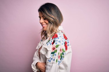 Moda kıyafetleri giyen genç ve güzel bir kadın. Manken, sokak tarzı giyiniyor. Pembe arka planda dikiliyor.