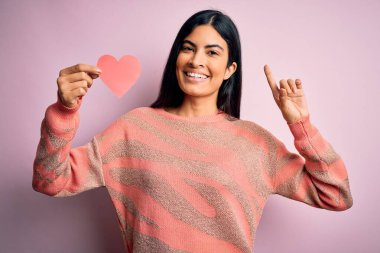 Pembe arka planda romantik kalp kâğıdı şekilli genç, İspanyol bir kadın bir fikir ya da soru işareti ile şaşırmış, mutlu bir yüz, bir numara