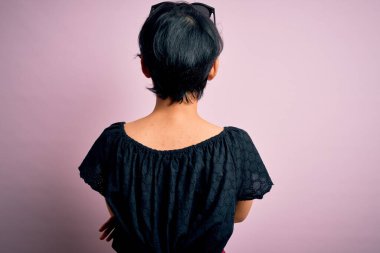 Genç, güzel Asyalı bir kız. Sıradan bir elbise giymiş. Soyutlanmış pembe arka planda duruyor.