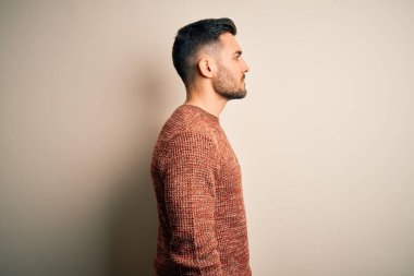 İzole edilmiş beyaz arka plan üzerinde duran, rahat profil pozu veren, doğal yüzlü ve kendinden emin gülümseyen genç, yakışıklı bir adam..