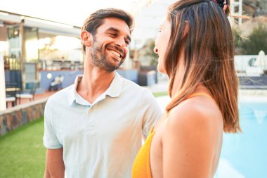 Tatilde mutlu ve kendinden emin gülümseyen genç bir çift. Yüzünde tebessümle plaj kulübünde sarılırken