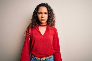 Kıvırcık saçlı, sıradan tişörtlü, beyaz arka planda duran, yüzünde ciddi bir ifade olan genç ve güzel bir kadın. Basit ve doğal bir şekilde kameraya bakıyorsun..