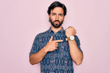 Pembe arka planda hippi tarzı giyinmiş genç, Latin asıllı bohem bir adam. Aceleyle saati, sabırsızlığı ve rahat bir ifadeyle kameraya bakıyor.