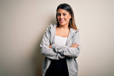 Genç, güzel, esmer, sporcu bir kadın beyaz arka planda antrenman yaparken kollarını kavuşturup kameraya bakarken gülümsüyor. Pozitif kişi.