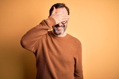 Sarı arka planda kahverengi süveter ve gözlük takan orta yaşlı, beyaz bir adam. Gülümsüyor ve yüzünde şaşkınlıktan gözleri kapayarak gülüyor. Kör kavram.