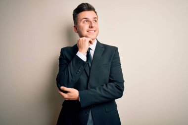 Zarif bir takım elbise giyen yakışıklı bir iş adamı ve izole edilmiş arka planda elleri çenesinde soru sorarken düşünceli bir ifade takınıyor. Gülen ve düşünceli bir yüz. Şüphe kavramı.