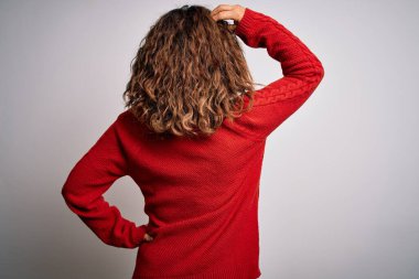 Orta yaşlı esmer kadın, sıradan bir süveter giyiyor. İzole edilmiş beyaz arka planda dikiliyor. Elleri kafasında şüpheyi düşünüyor.