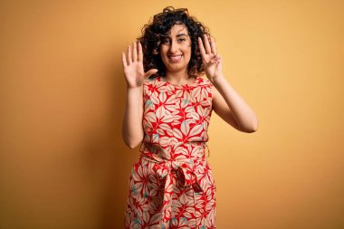 Genç ve güzel kıvırcık Arap kadın tatilde. Çiçekli bir elbise ve güneş gözlüğü takıyor. Sekiz numaralı parmaklarıyla işaret ediyor..