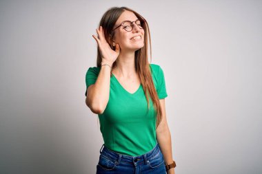 Genç, güzel, kızıl saçlı bir kadın, günlük yeşil tişört ve gözlük takıp beyaz arka planda sırıtarak dedikodu ve dedikoduları dinliyor. Sağırlık kavramı.