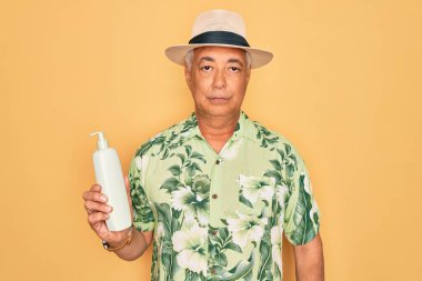 Orta yaşlı, kır saçlı, yaz şapkası takan, elinde güneş kremi tutan zeki yüzlü, ciddi düşünen, kendinden emin bir adam.