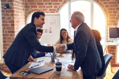 Bir grup iş adamı toplantıda mutlu ve kendinden emin gülümsüyor. Ofiste anlaşmak için el sıkışırken gülümseyerek konuşmak..