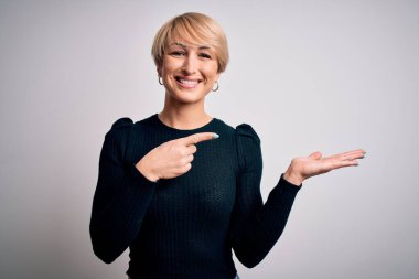 Modern kısa saç stili olan genç, sarışın bir kadın izole edilmiş arka planda durup kameraya hayret ediyor ve gülümsüyor..