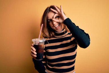 Genç, güzel esmer kadın kola bardağıyla içki içiyor mutlu yüzlü saman kullanıyor tamam işaret veriyor parmaklarının arasından bakıyor.