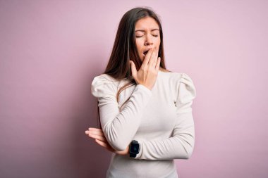 Mavi gözlü genç bir kadın pembe arka planda sıradan beyaz tişörtler giyip ağzıyla esnemekten sıkılmış. Huzursuz ve uykulu..