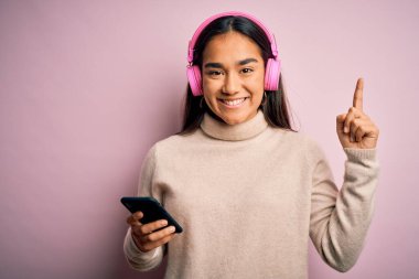 Akıllı telefon ve kulaklık kullanarak müzik dinleyen genç ve güzel Asyalı bir kadın bir fikir veya soru işareti ile şaşırdı.