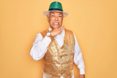 Orta yaşlı, yaşlı, kır saçlı, Brezilya karnavalı kıyafeti giyen, sarı arka planda, boğazı bıçak gibi kesen, saldırganlığı şiddetle tehdit eden bir adam.
