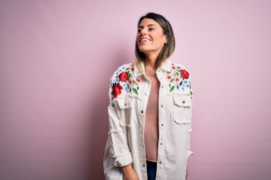 Moda kıyafetleri giyen genç ve güzel bir kadın. Manken, sokak tarzı giyiniyor. Pembe arka planda dikiliyor.