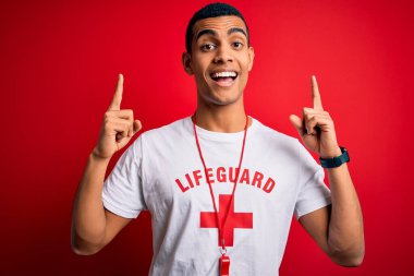 Genç ve yakışıklı Afro-Amerikalı cankurtaran kırmızı haçlı tişört giyiyor ve ıslık çalıyor. Şaşırmış, şaşırmış ve parmaklarıyla işaret ediyor ve kollarını kaldırıyor..