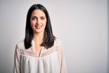 Mavi gözlü genç esmer kadın izole edilmiş beyaz arka plan üzerine günlük tişört giyiyor ve yüzünde mutlu ve havalı bir gülümseme var. Şanslı kişi..