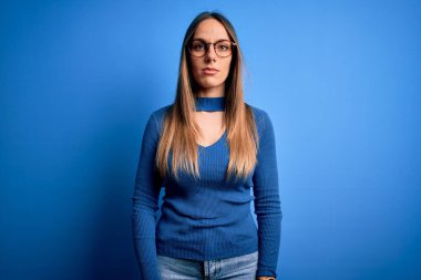 Mavi gözlüklü, mavi arka planda duran güzel sarışın kadın yüzünde ciddi bir ifadeyle rahatlamış. Basit ve doğal bir şekilde kameraya bakıyorsun..