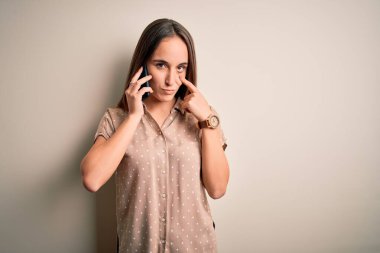 Genç, güzel bir kadın, beyaz arka planda akıllı telefondan konuşuyor. Gözünü dikip jestini izliyor. Şüpheli bir ifade.