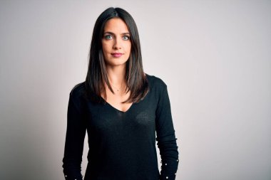 Mavi gözlü, esmer bir kadın beyaz arka planda siyah bir süveter giyiyor ve yüzünde ciddi bir ifade var. Basit ve doğal bir şekilde kameraya bakıyorsun..