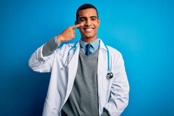 英俊的非洲裔美国医生 身穿外套和听诊器 头戴蓝色背景 手指手画脚 面面相觑 面带微笑 美的概念 — 图库照片