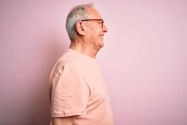 Grey haired senior man wearing glasses standing over pink isolated background looking to side, relax profile pose with natural face with confident smile.