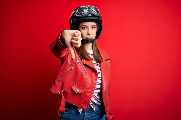 若い美しいブルネットのオートバイのヘルメットと赤いジャケットを身に着けているオートバイの女性は 親指ダウンジェスチャーで不満と否定的な拒絶と怒りを示すように見えます 悪い表現 — ストック写真