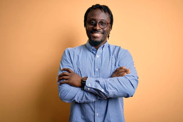 Young handsome african american man wearing shirt and glasses over yellow background happy face smiling with crossed arms looking at the camera. Positive person.