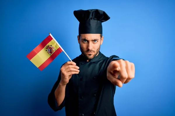若いですハンサムな炊飯器男ひげを身に着けている制服を保持スペイン語の旗を指差す指でカメラとあなたに 手のサイン 正とフロントから自信を持ってジェスチャー — ストック写真
